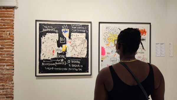 A Black woman looking at displayed art works by Jean-Michel Basquiat