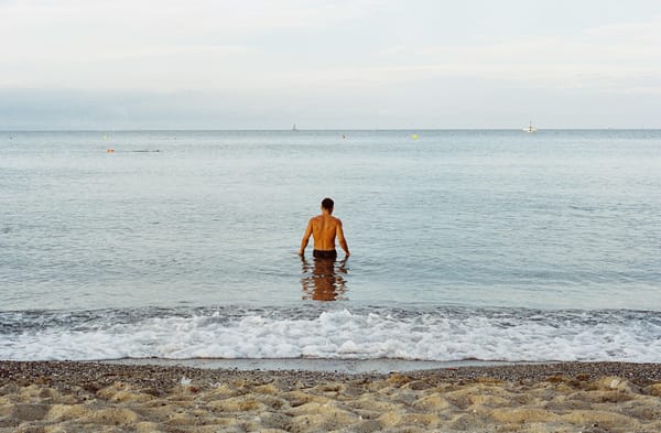 a lone man waist deep in the sea, facing towards the sky, the photograph is behind him.